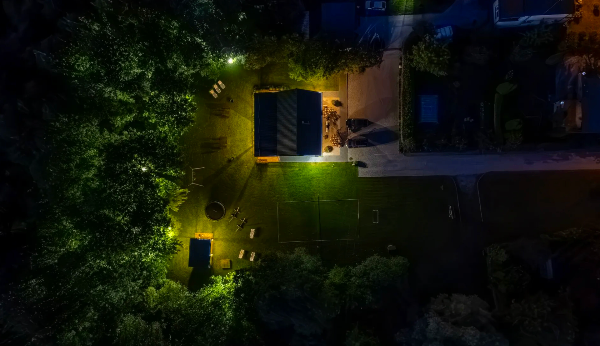 Widok z lotu ptaka nocą — oświetlony ogród i domek